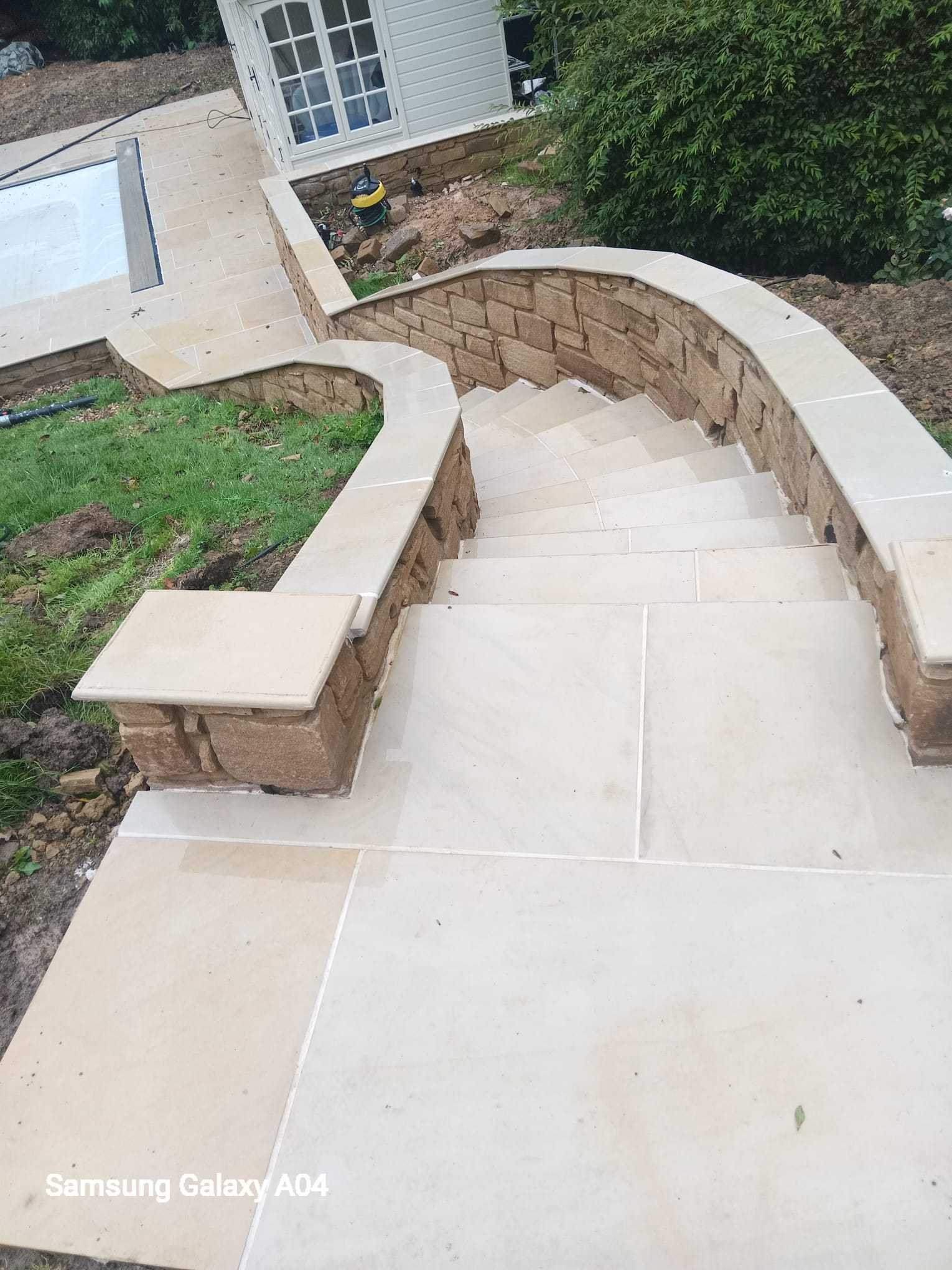 Curved sandstone garden staircase with capped stone walls climbing to a house