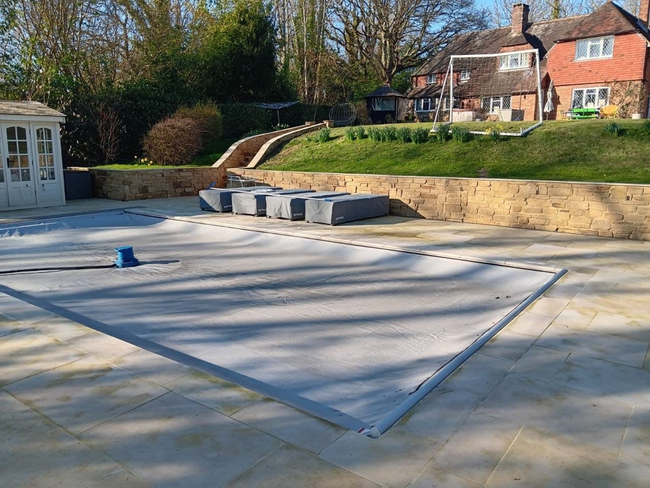 Covered swimming pool set within a broad sandstone patio surround