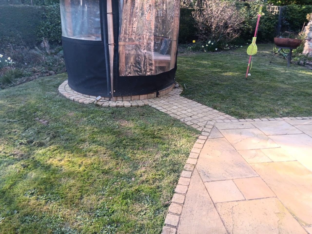 Block-paved path with sandstone edging curving around a garden pod