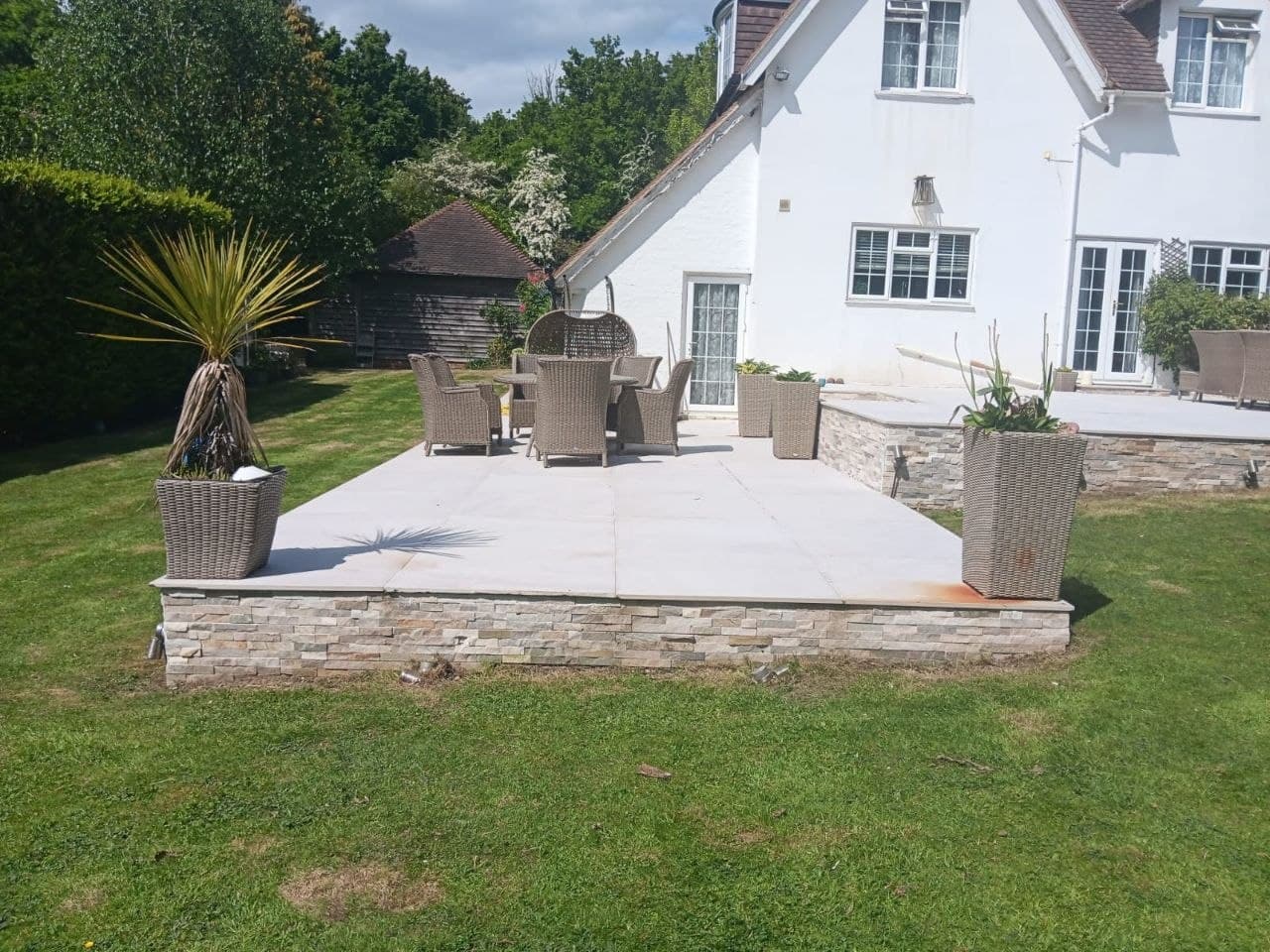 Raised porcelain terrace with natural stone facing and planters at a white cottage