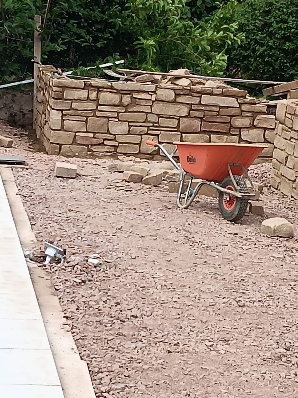 Neatly coursed natural stone wall under construction with tools on site
