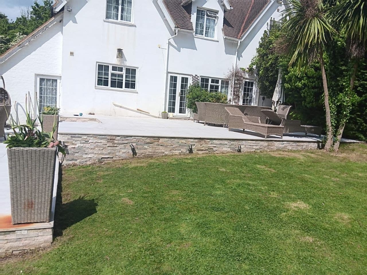 Raised porcelain terrace on a natural stone-clad wall behind a white period house