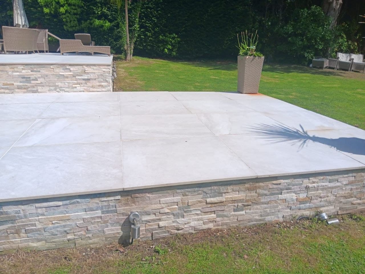 Raised porcelain terrace on a stacked-stone clad wall with lawn beyond