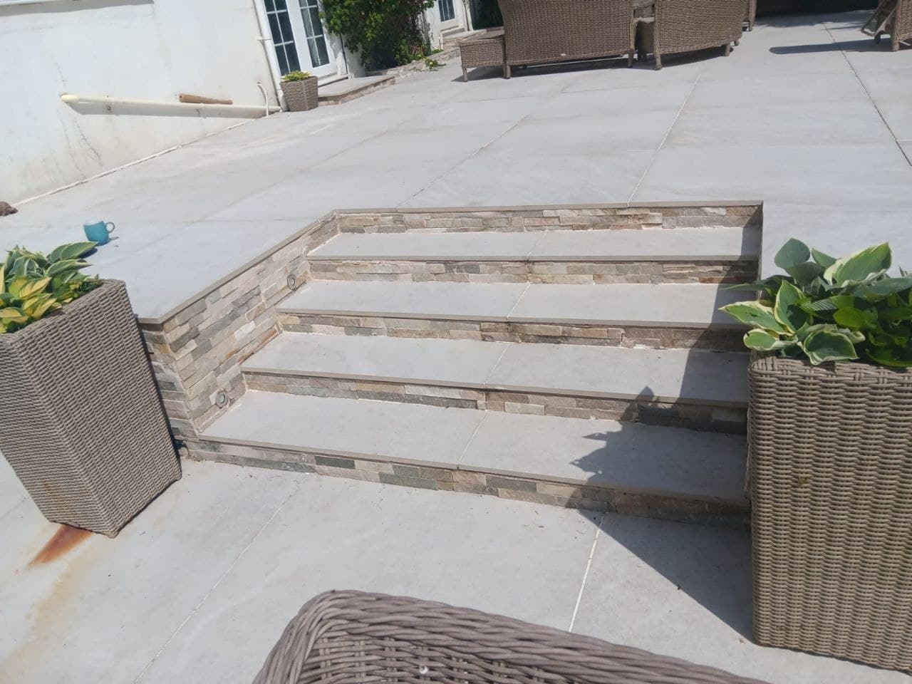 Wide porcelain terrace with stone-faced steps and hosta-filled planters