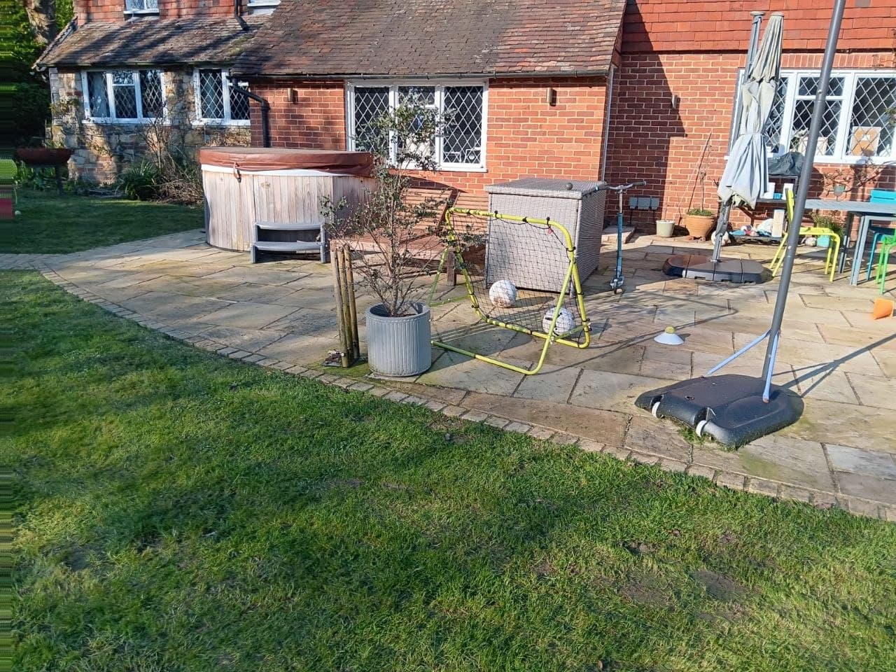 Sandstone patio with hot tub and seating beside a period brick and stone home