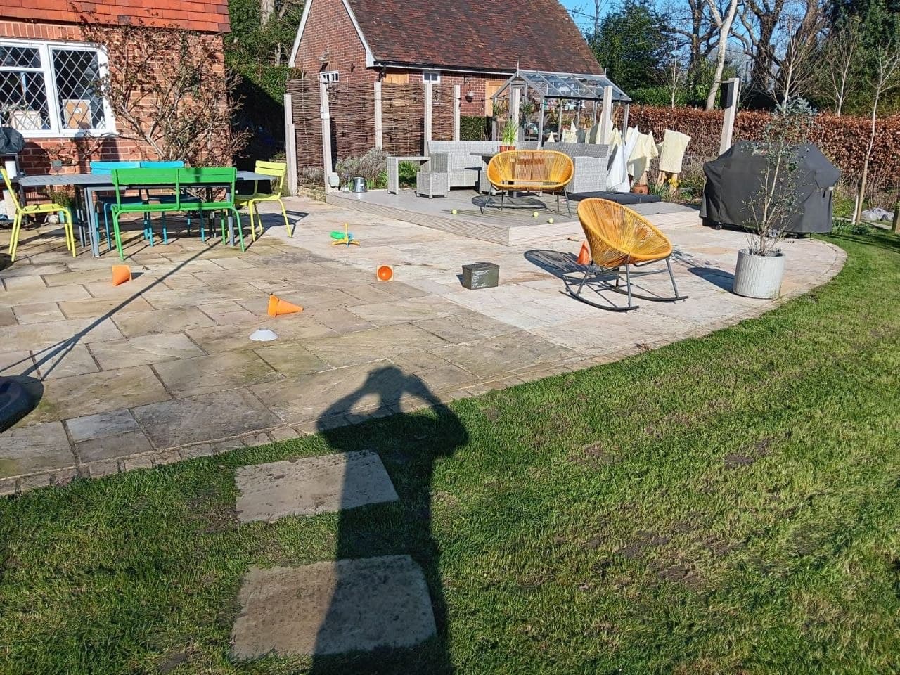 Sandstone patio with pergola seating area and lawn beside a tiled-roof house